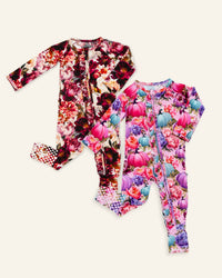 Two long-sleeve baby footed one-piece sleepers with front zippers, displayed flat on a light cream background. The sleeper on the left features a dark floral pattern with red, pink, and purple flowers.